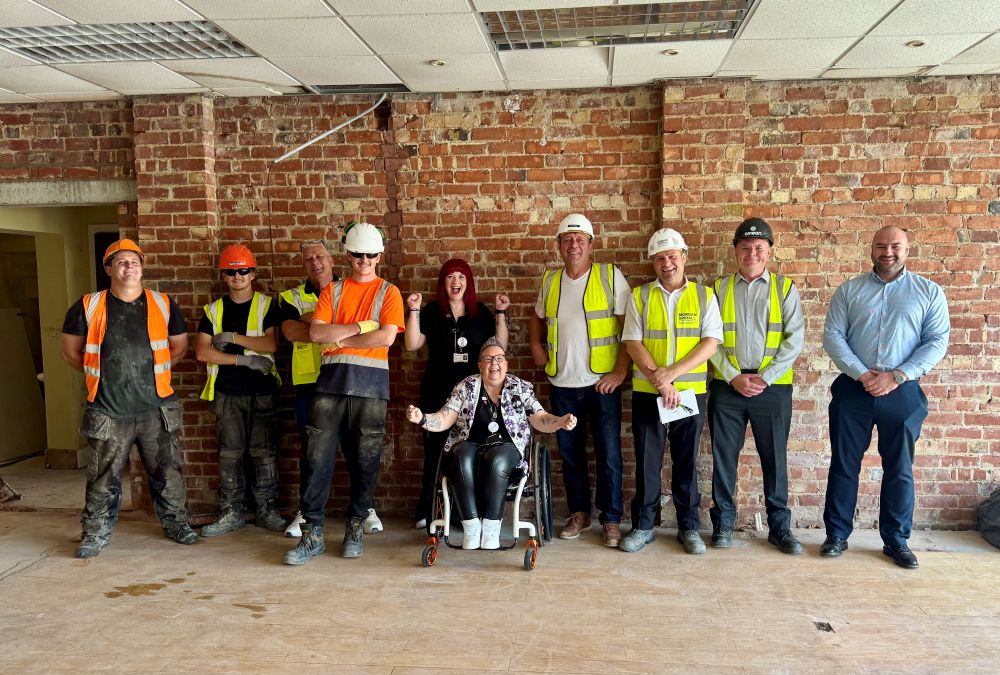 A group of construction workers in high-vis joined by man in smart office wear and woman in wheelchair.
